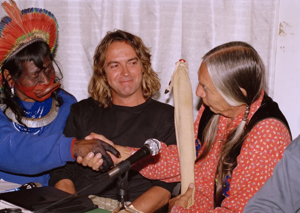 Chief Raoni, left, of the Indigenous Kayapo Nation in Brazil, left, and Native American Indian Red Crow, right, of South Dakota, shake hands during a press conference to present a project for an environmental park in Brazil’s Amazon, as Belgian filmmaker Jean-Pierre Dutilleux, who is participating in the project, sits between them.