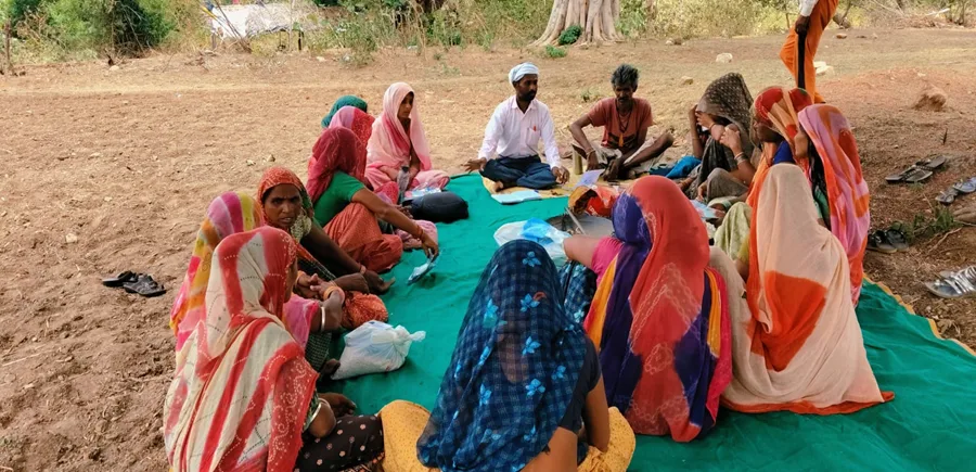 Kalawati sits in on a Saksham Samuh gathering under a tree on the village outskirts, where facilitator Manilal Damor and fellow farmers discuss sustainable farming and livestock practices.