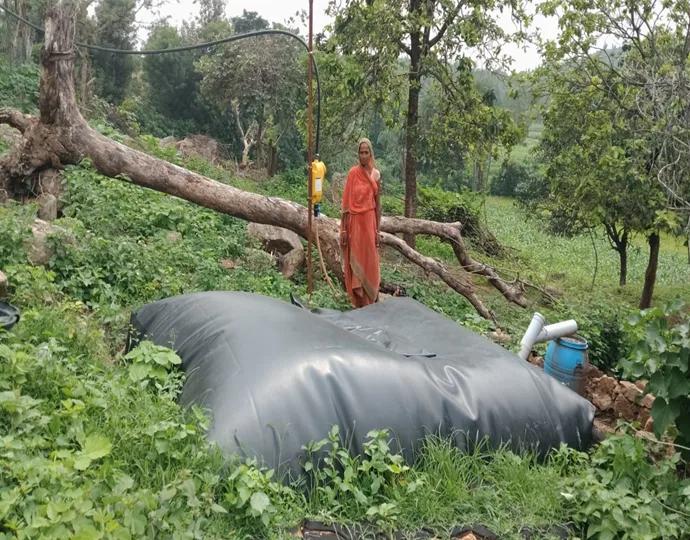 Kalawati beside the family's biogas digester, installed with Vaagdhara's technical support it now meets all the household's cooking-fuel needs.